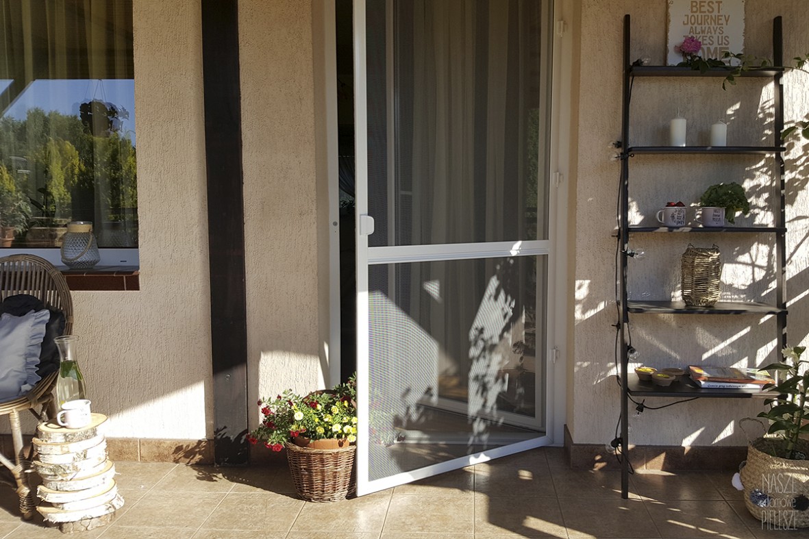Biała aluminiowa moskitiera drzwiowa na zawiasach samodomykających oraz magnesach zamontowana na drzwiach tarasowych.