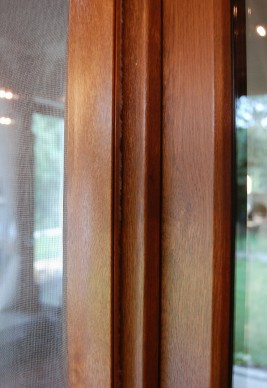 Profil aluminiowy w okleinie drewnopodobnej oraz z uszczelką szczotkową drzwi moskitierach przylegający do ramy okiennej.